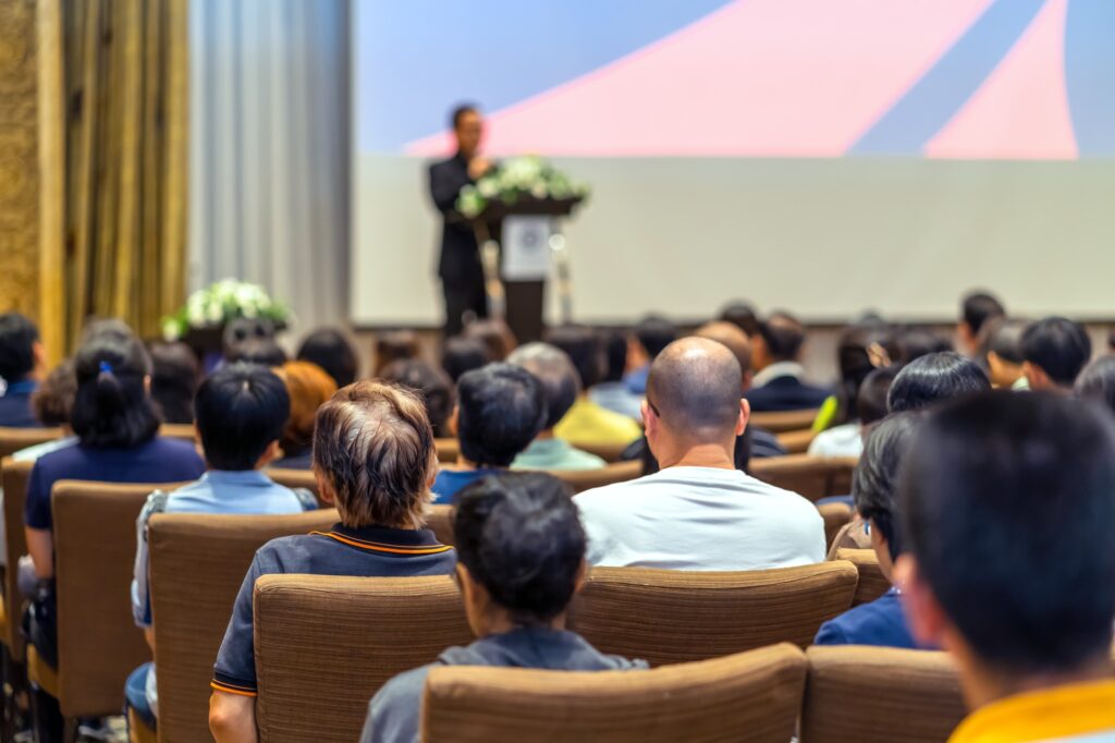 Back side of audience listening the Speaker with podium on the stage in the conference hall